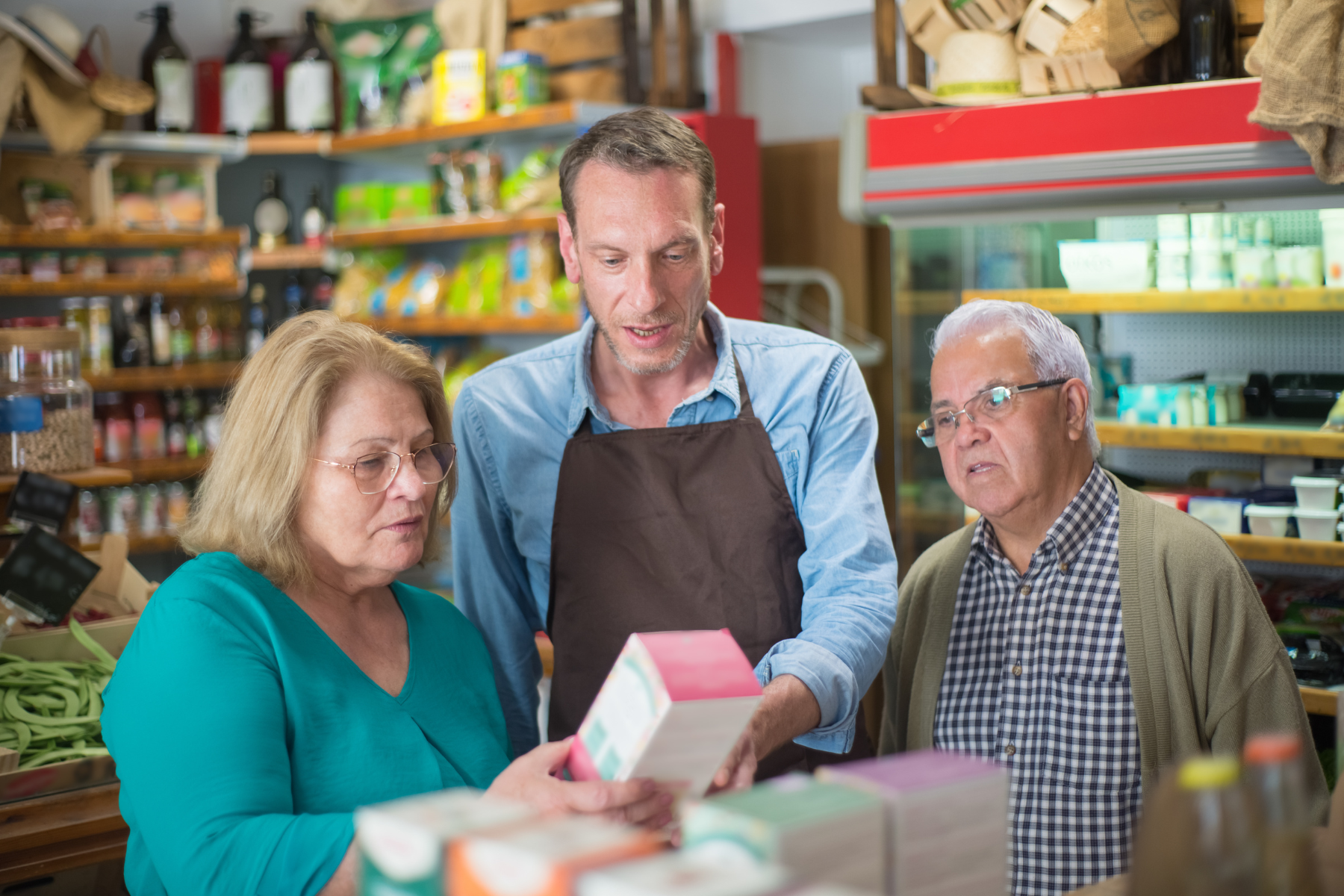 Older white couple discussing a product with a shop keeper in brown apron.