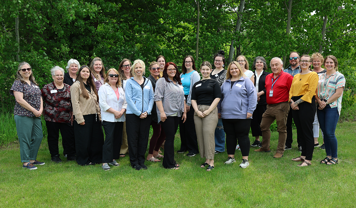 All staff summer 2025_retouched_cropped_72 Group of adults posing outside and smiling at the camera.