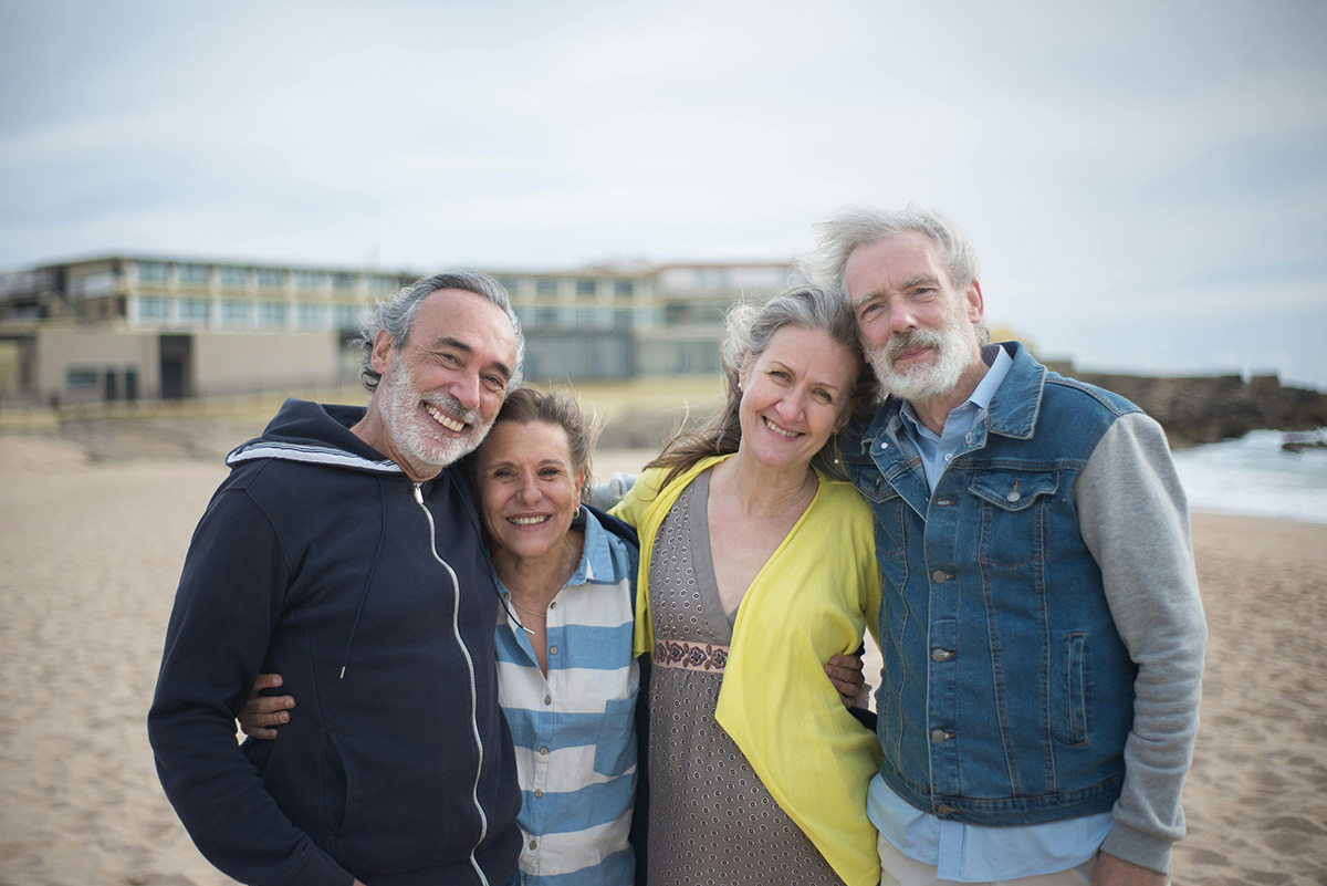 Two older couples side hugging while at the beach