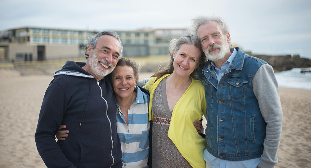 Two older couples side hugging while at the beach