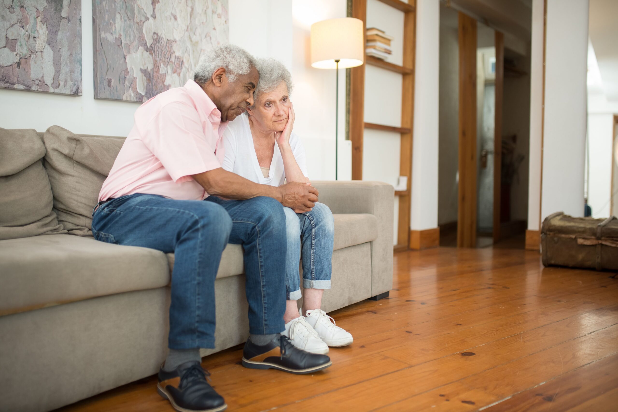 two older adults seated on a couch in their living room looking concerned
