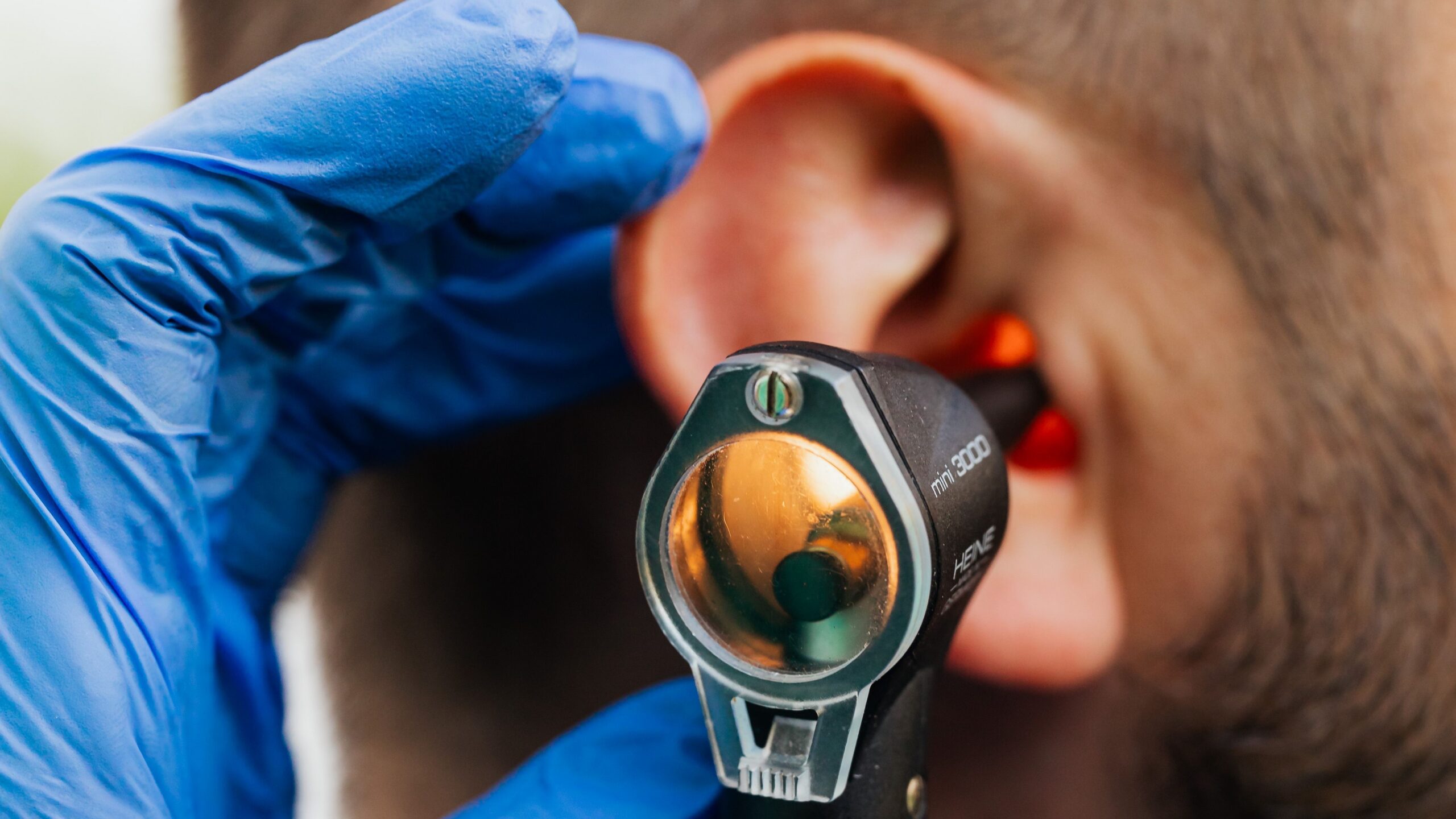 a gloved hand using an otoscope in a patient's ear